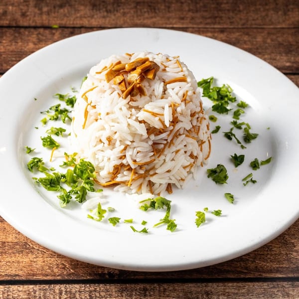 A mound of white rice with vermicelli and chopped parsley on a white plate.