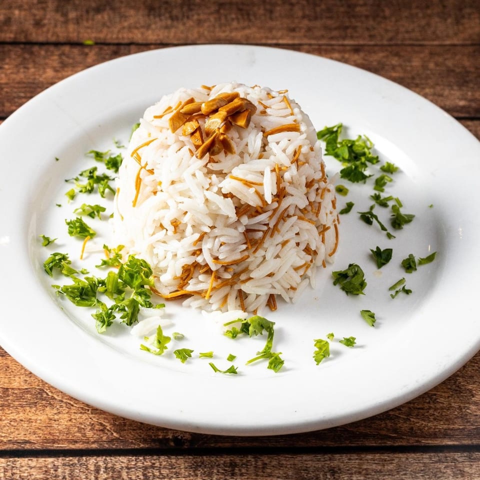 A mound of white rice with vermicelli and toasted almonds, garnished with parsley on a white plate.