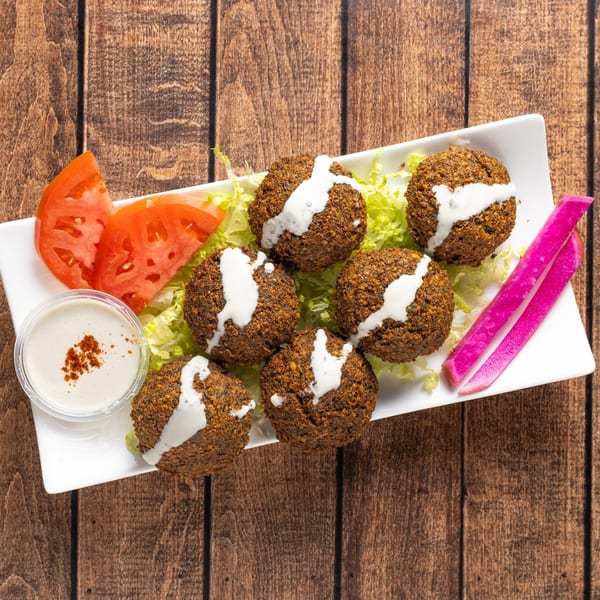 Shawarmaz falafel plate with six falafel, lettuce, tomato, pickled turnips, and tahini sauce.