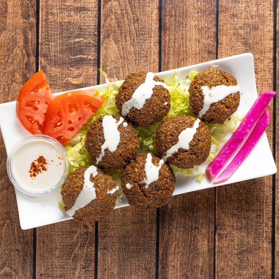 Six falafel balls drizzled with white sauce, served with lettuce, tomato, and pickled turnips.