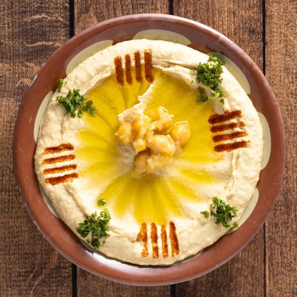 Creamy hummus drizzled with olive oil, topped with chickpeas and fresh parsley, on a rustic plate.